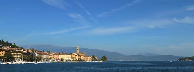 Trip Holland beliebte Urlaubsziele am Gardasee -  Mit einer Fläche von 370 km² ist der Gardasee der größte See Italiens. Es liegt am Fuße der Alpen und erstreckt sich über drei Staaten: Lombardei, Venetien und Trentino. Die maximale Tiefe des Sees beträgt 346 m, er hat eine längliche Form und sein nördliches Ende ist sehr schmal. Dort ist der See von den Bergen der Gruppo di Baldo umgeben. Du trittst aus deinem gemütlichen Hotelzimmer und es begrüßt dich die warme italienische Sonne. Du blickst auf den atemberaubenden Gardasee, der in zahlreichen Blautönen schimmert - von tiefem Dunkelblau bis zu funkelndem Türkis. Majestätische Berge umgeben dich, während die Brise sanft deine Haut streichelt und der Duft von blühenden Zitronenbäumen deine Nase kitzelt. Du schlenderst die malerischen, engen Gassen entlang, vorbei an farbenfrohen, blumengeschmückten Häusern. Vereinzelt unterbricht das fröhliche Lachen der Einheimischen die friedvolle Stille. Du fühlst dich wie in einem Traum, der nicht enden will. Jeder Schritt führt dich zu neuen Entdeckungen und Abenteuern. Du probierst die köstliche italienische Küche mit ihren frischen Zutaten und verführerischen Aromen. Die Sonne geht langsam unter und taucht den Himmel in ein leuchtendes Orange-rot - ein spektakulärer Anblick.